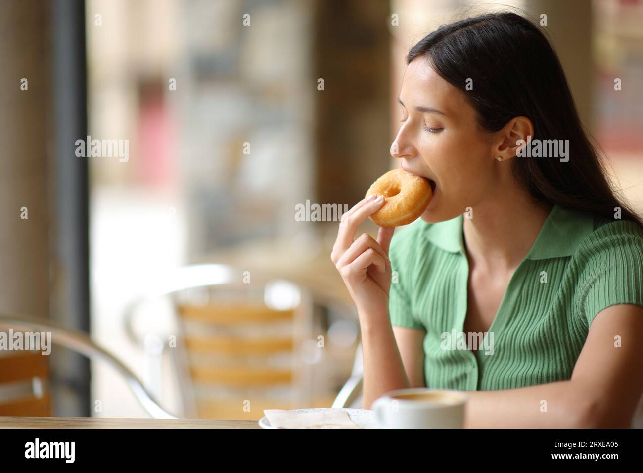 Frau auf einer Restaurantterrasse, die Donut zum Frühstück isst Stockfoto