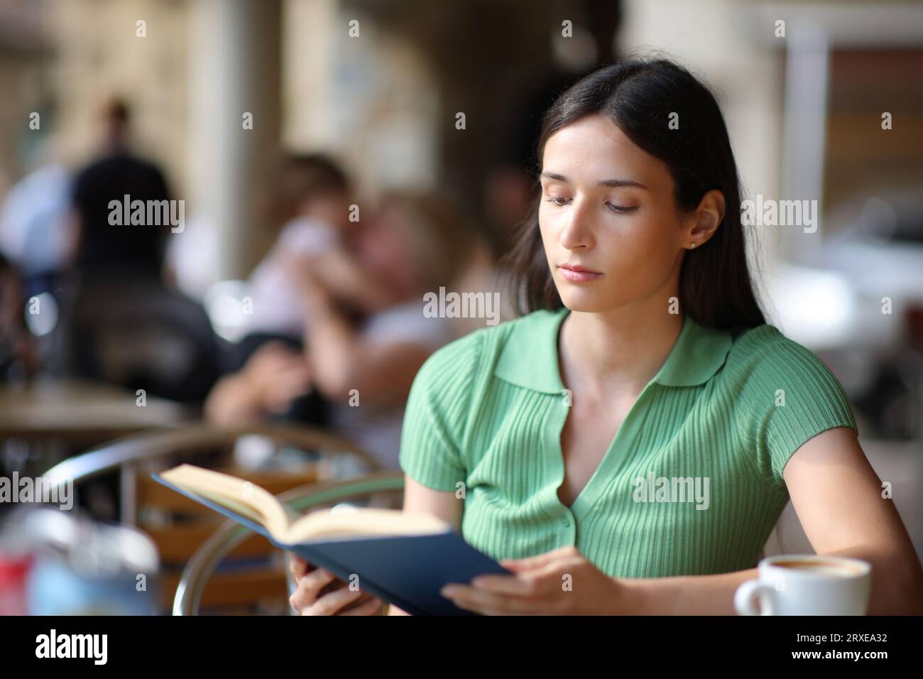 Eine ernsthafte Frau liest ein Buch, das auf der Terrasse eines Coffee Shops sitzt Stockfoto