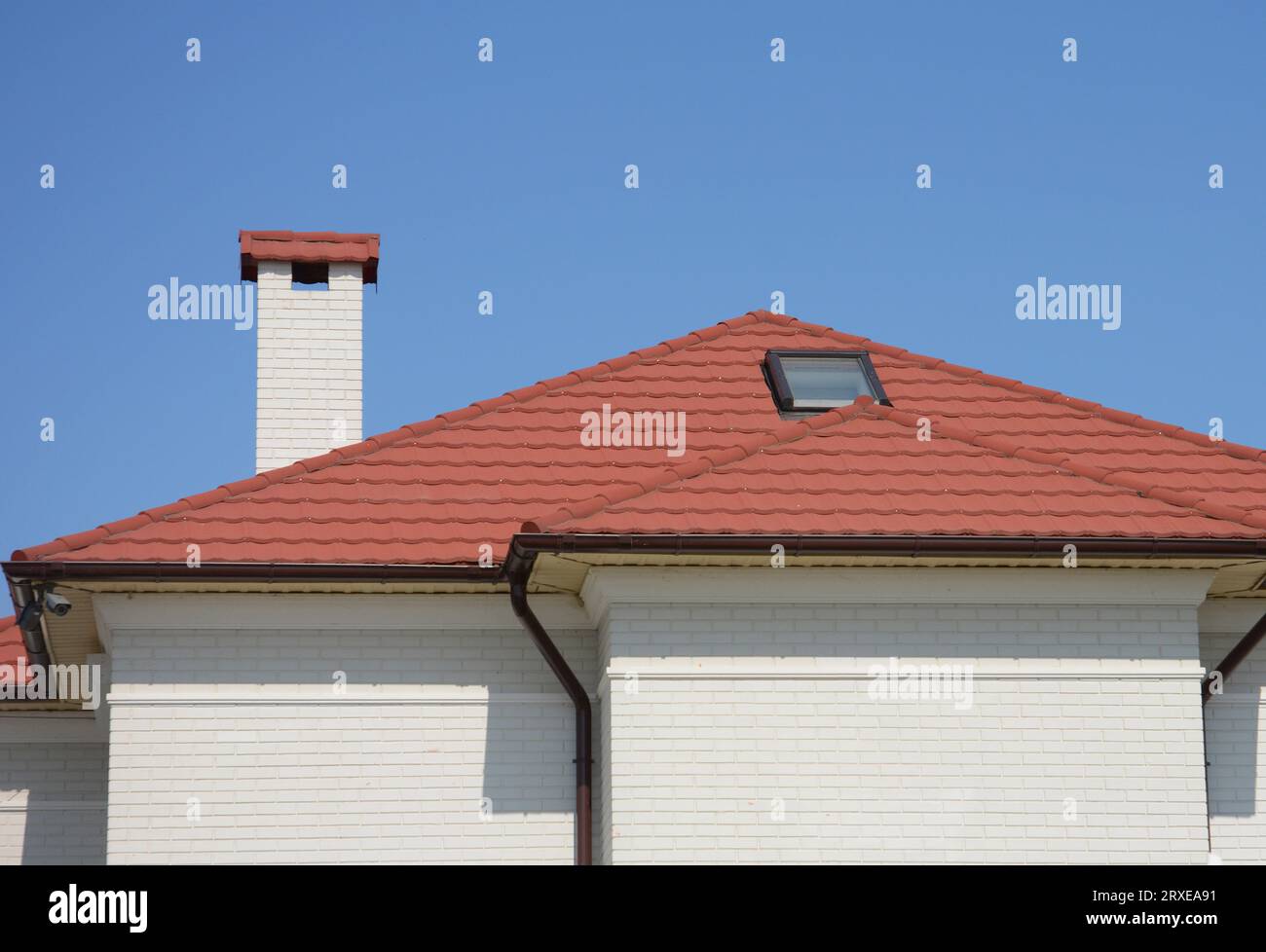 Das Dach des Hauses besteht aus roten Keramikfliesen mit Dachfenster, Regenrinne und weißen Backsteinfassaden. Stockfoto