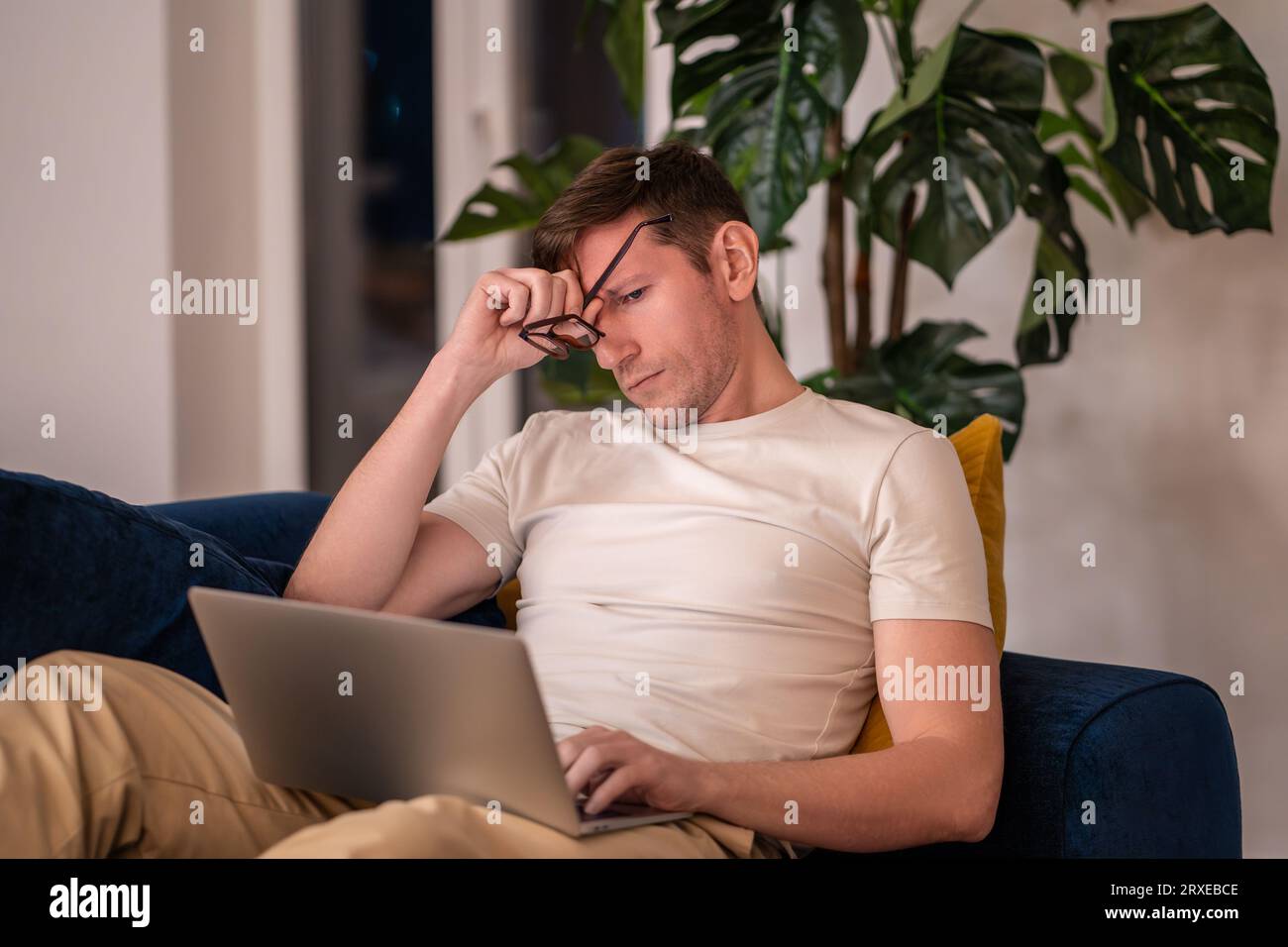 Müder, verschlafener Mann, der sich die Augen reibt und abends zu Hause auf dem Laptop sitzt. Stockfoto