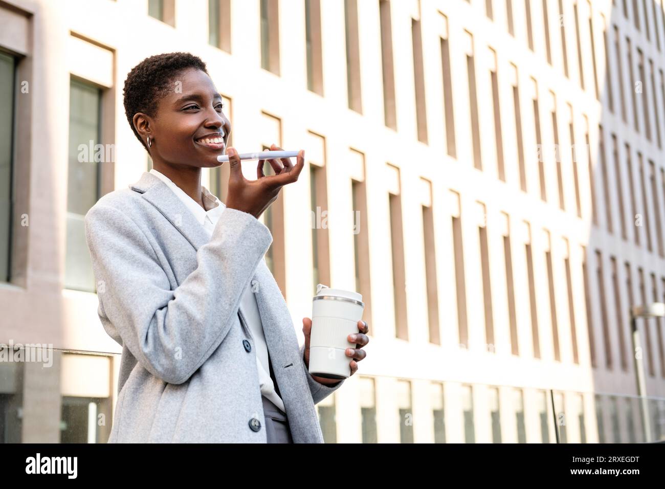 Horizontales Porträt einer attraktiven jungen afrikanerin, die telefonisch eine Sprachnachricht sendet. Sie steht in der Nähe von Tribunal-Gebäuden Stockfoto