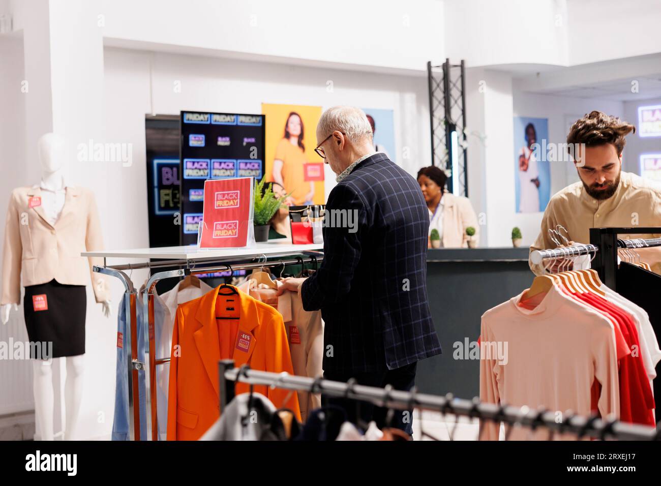 Die Verbraucher schauen sich Kleidung mit roten Preisschildern an, die an Regalen hängen, und kaufen während des Black Friday-Verkaufs im Bekleidungsgeschäft ein. Kunden können sich über saisonale Angebote und Sonderangebote im Einkaufszentrum informieren Stockfoto