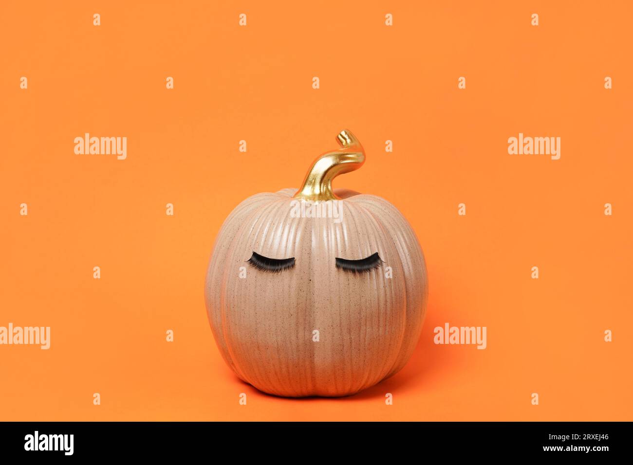 Halloween Kürbis mit falschen Wimpern auf hellem orangem Hintergrund. Herbst, Herbst, Schönheitskonzept. Leerzeichen kopieren Stockfoto