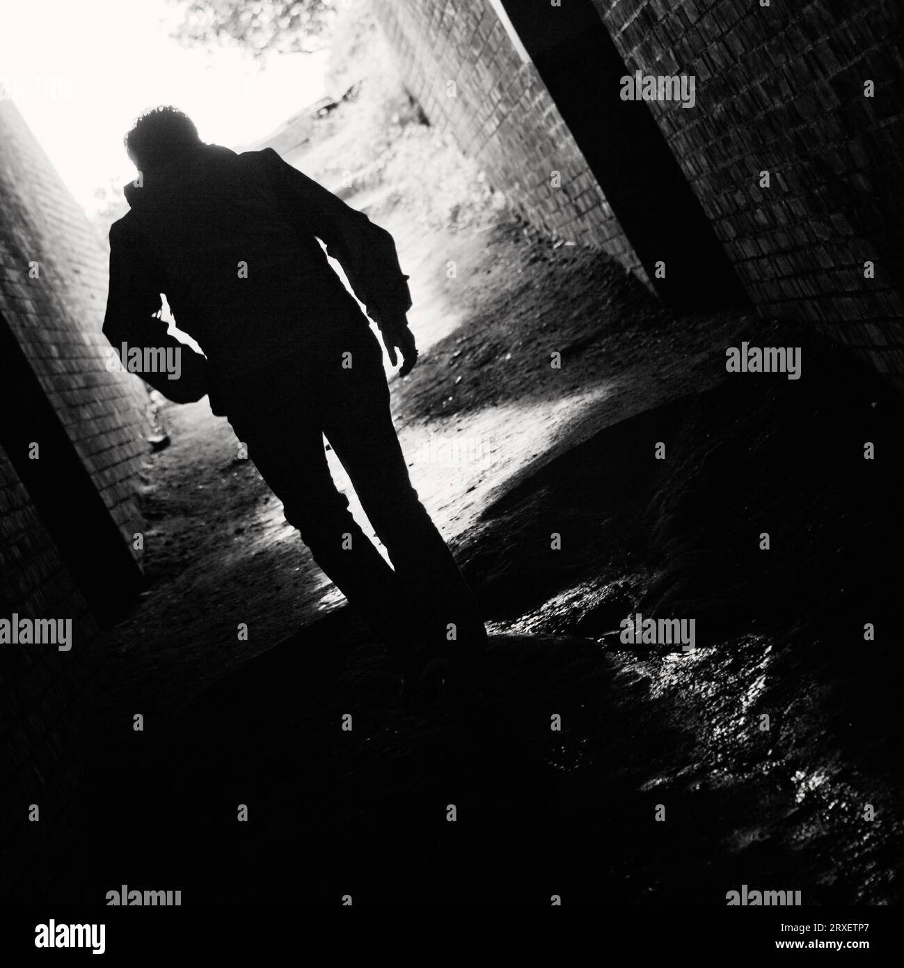 Rückansicht einer Person, die durch einen dunklen Tunnel geht. Stockfoto