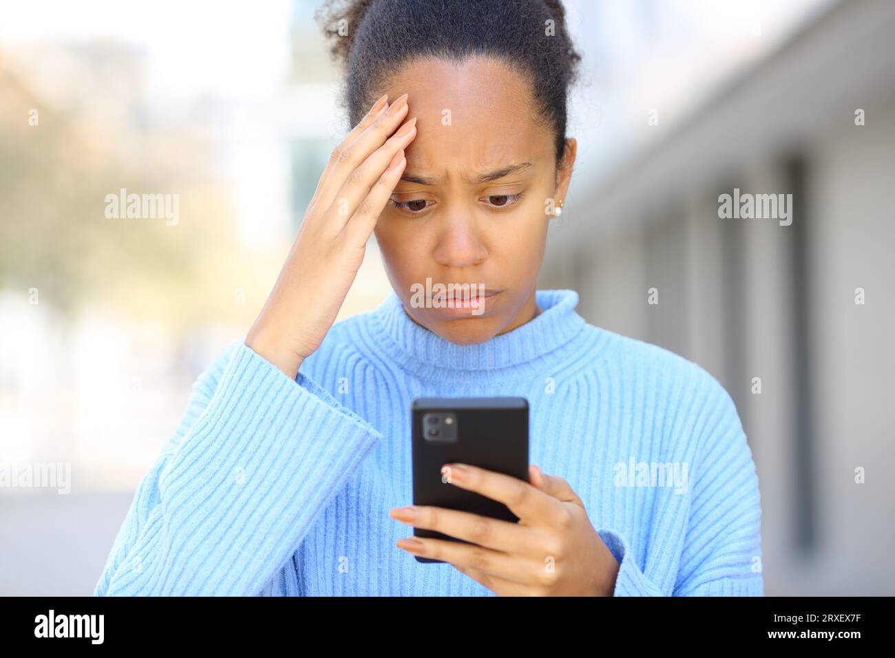 Vorderansicht eines Porträts einer besorgten schwarzen Frau, die schlechte Nachrichten am Telefon auf der Straße überprüft Stockfoto