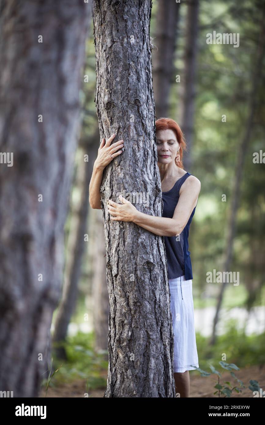 Ältere Frau mit geschlossenen Augen umarmt einen Baum Stockfoto
