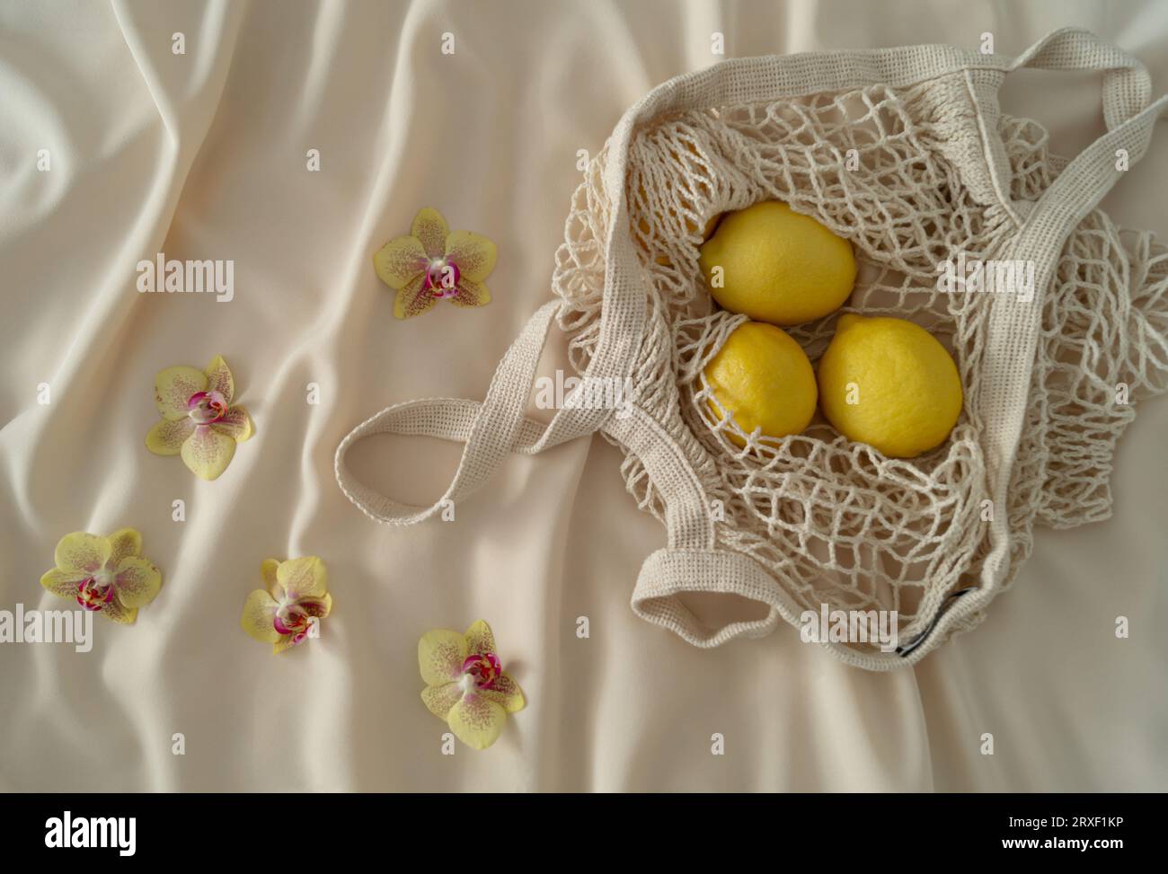 Flach liegende tropische Orchideen und Zitronen in Häkelnettentasche. Ästhetische Sommeridee. Minimales kreatives Konzept. Stockfoto
