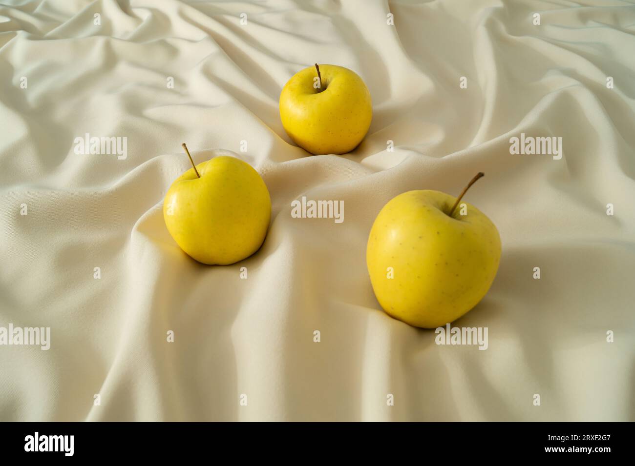 Gelbe Bio-Äpfel auf luxuriöser Sandseide. Gesunde Ernährung Idee. Minimales kreatives Konzept der Einfachheit. Stockfoto
