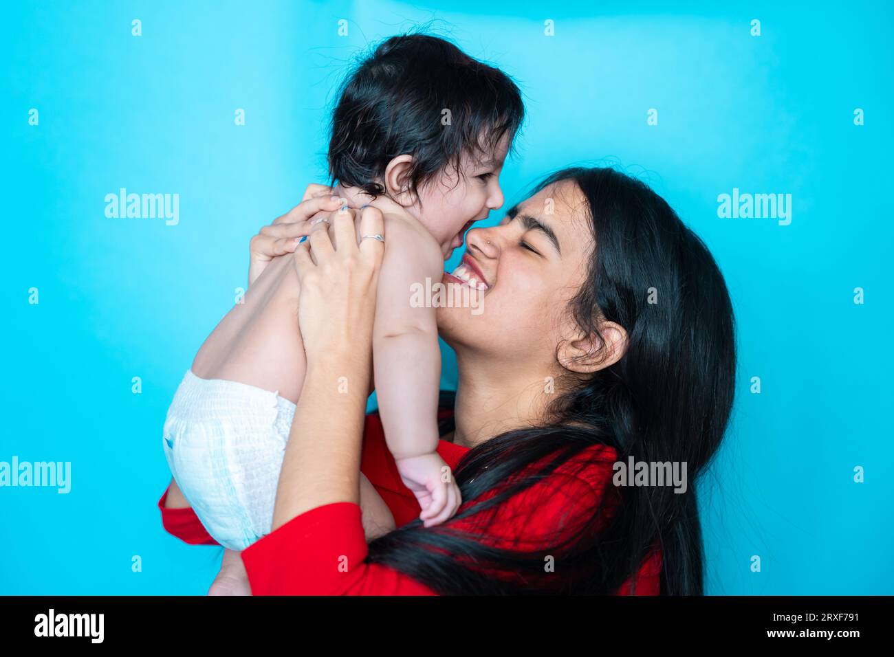 Indisches Teenager-Mädchen spielt sechs Monate süßes kleines Baby in Windel isoliert über blauem Hintergrund. Asiatisches Kleinkind und Schwester, glückliche Familie. Stockfoto