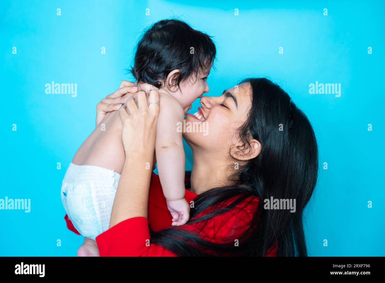 Indisches Teenager-Mädchen spielt sechs Monate süßes kleines Baby in Windel isoliert über blauem Hintergrund. Asiatisches Kleinkind und Schwester, glückliche Familie. Stockfoto