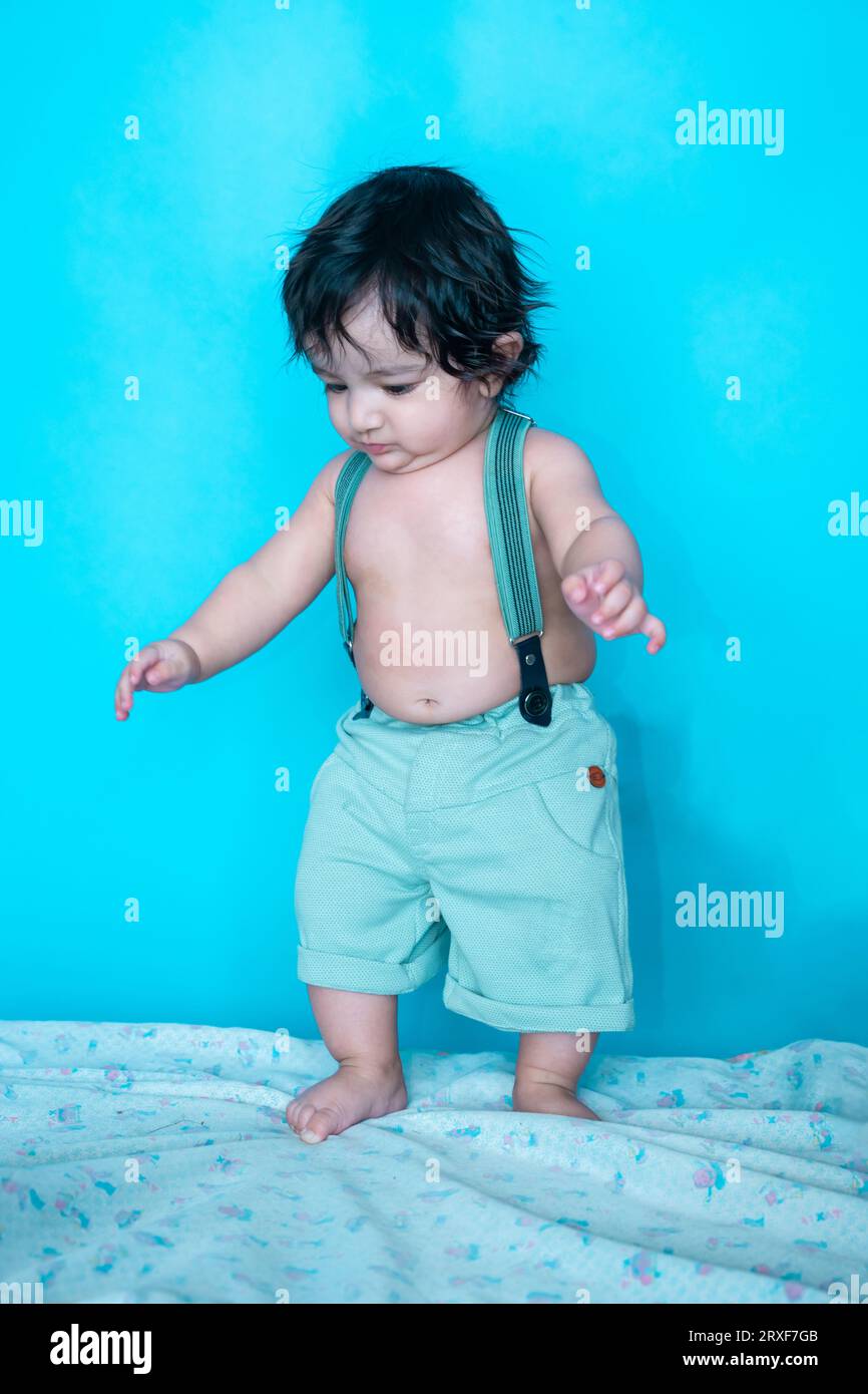 Lächelnder sechs Monate alter süßer indischer Junge, der versucht, isoliert über blauem Studiohintergrund, glückliches Kind mit schwarzem Haar. Stockfoto