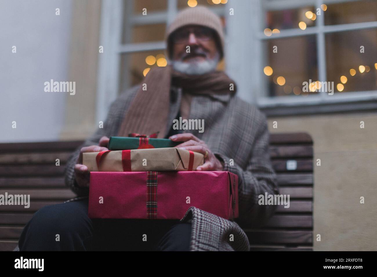 Älterer Mann sitzt auf einer Bank und hält viele Chrismtas-Geschenke in den Händen Stockfoto