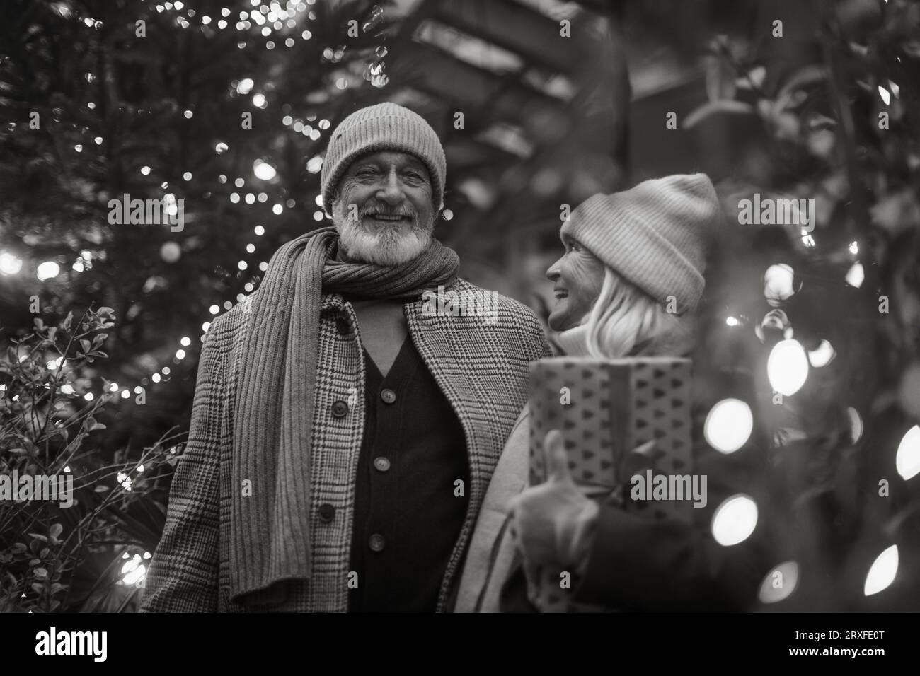 Schwarz-weißes Porträt eines älteren Paares, das den weihnachtsmarkt besucht, Geschenke und weihnachtsbaum kauft. Stockfoto