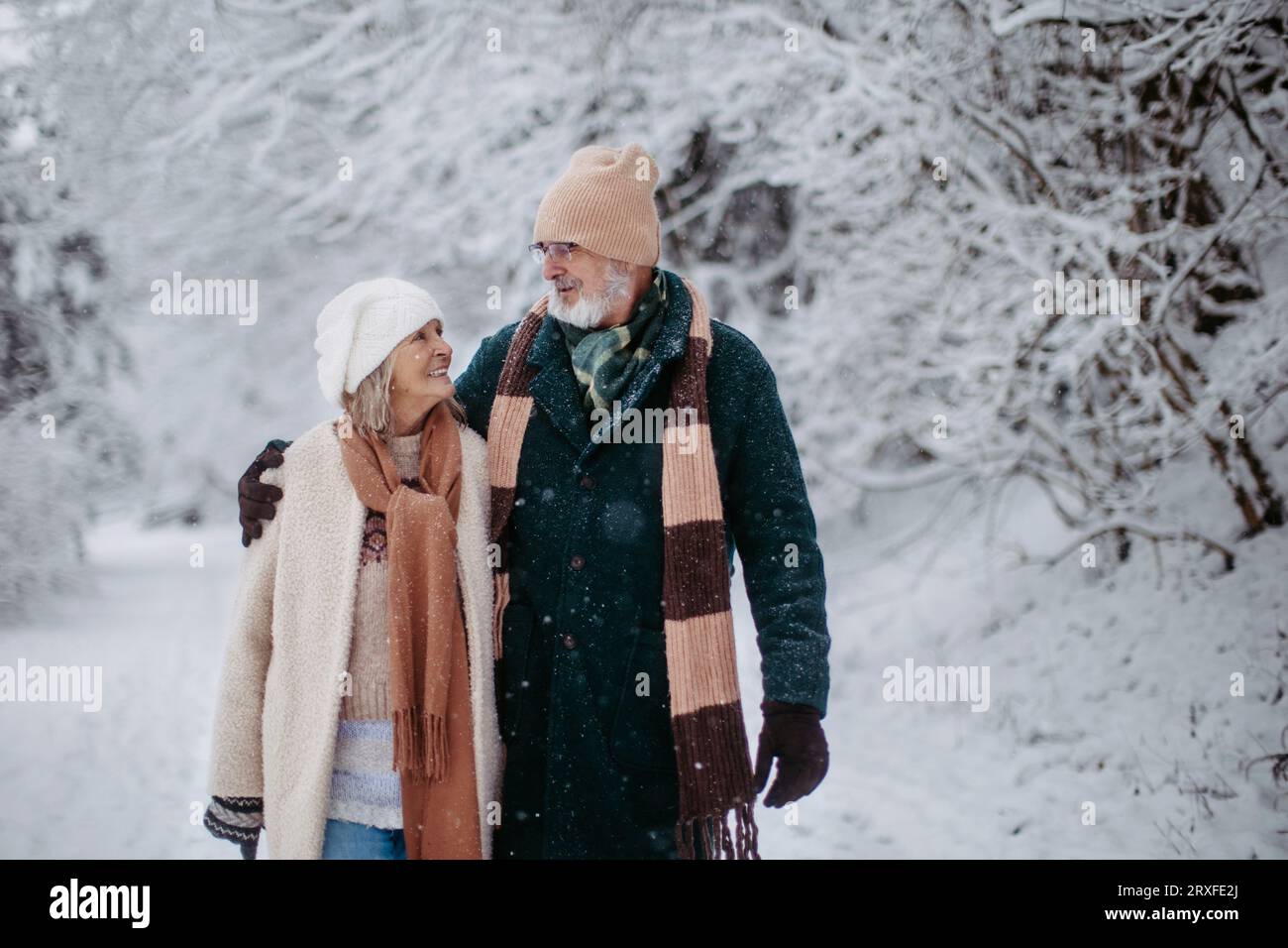Elegantes Seniorenpaar, das im verschneiten Park spaziert, während des kalten Winters. Stockfoto