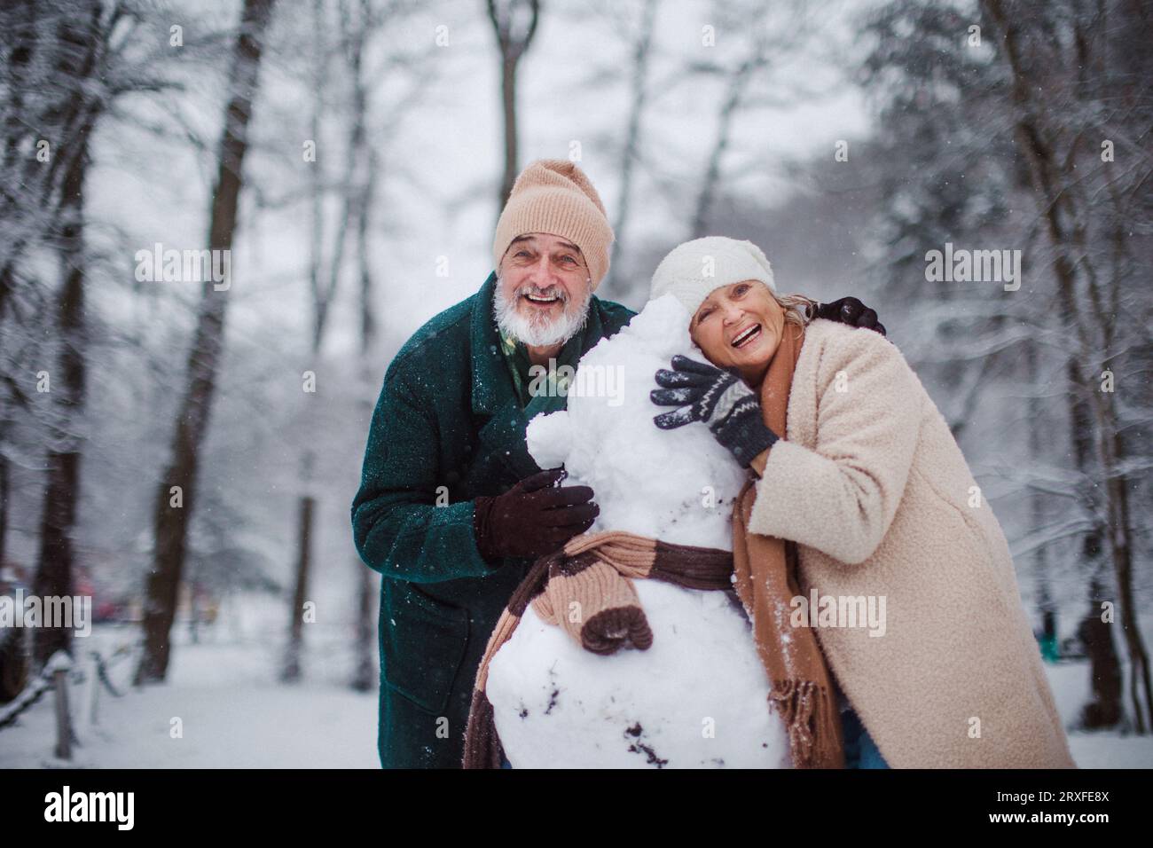 Elegantes Seniorenpaar, das Schneemann an einem kalten, schneebedeckten Wintertag baut. Stockfoto