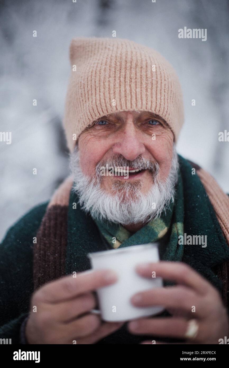 Porträt eines eleganten älteren Mannes, der während des kalten Winters an einem schneebedeckten Tag im Freien heißen Tee trinkt. Stockfoto