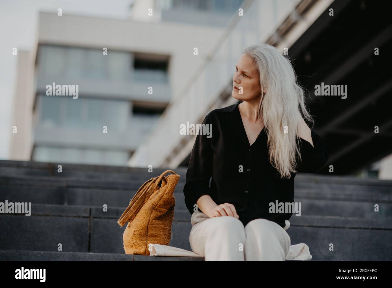 Porträt einer schönen Frau mit grauen Haaren, die auf Betontreppen in der Stadt sitzt und warmes Sommerwetter genießt. Stockfoto