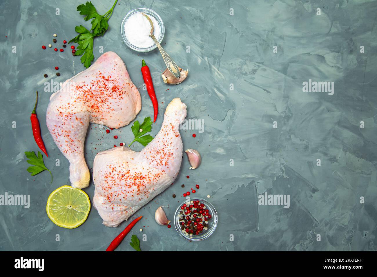 Rohe Hähnchenschenkel, Knoblauch, Chili, Zitrone und Kräuter auf grauem Hintergrund. Draufsicht. Stockfoto