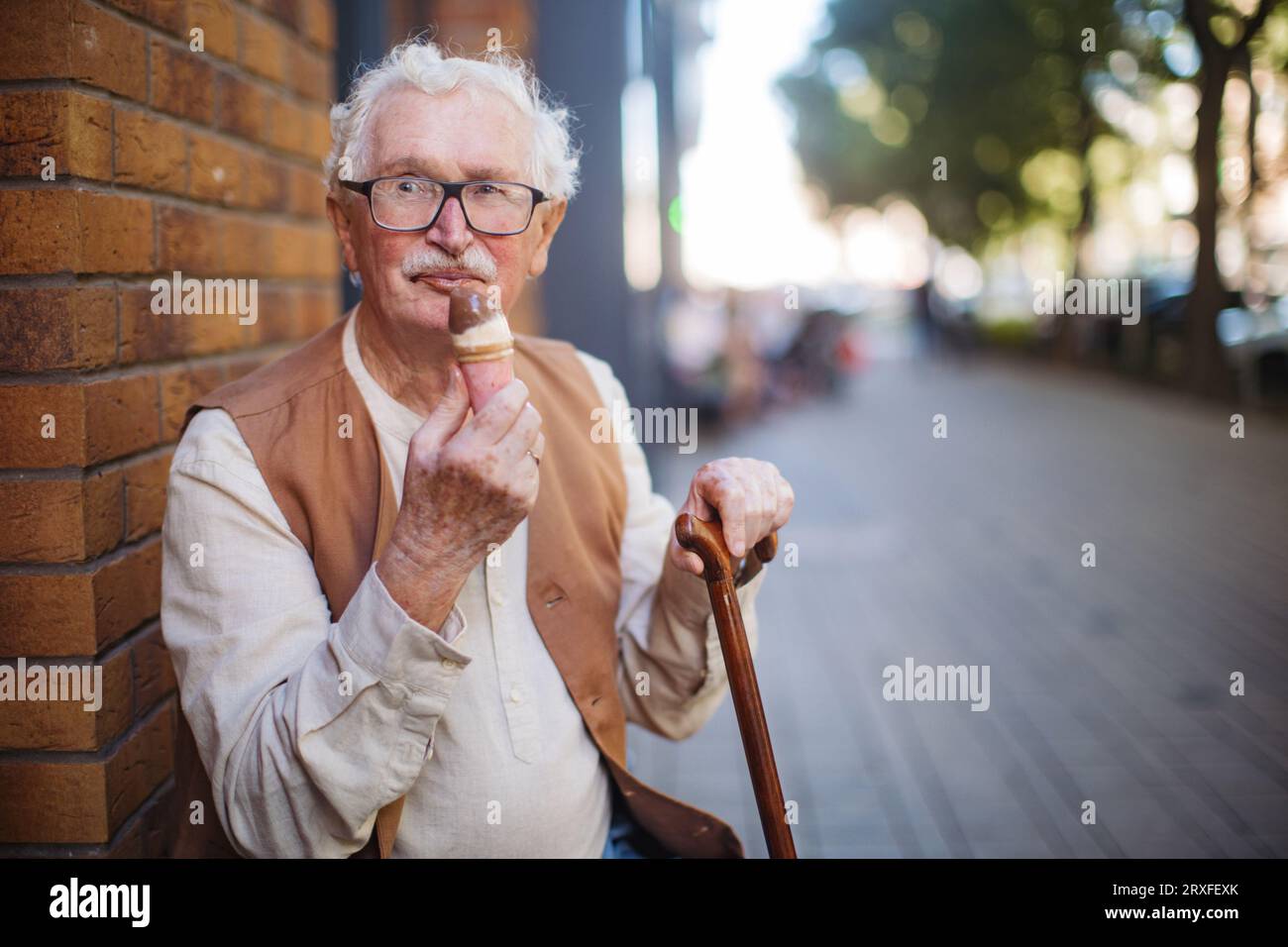 Porträt eines älteren Mannes mit Gehstock, der an einem heißen Sommertag Eis isst. Stockfoto