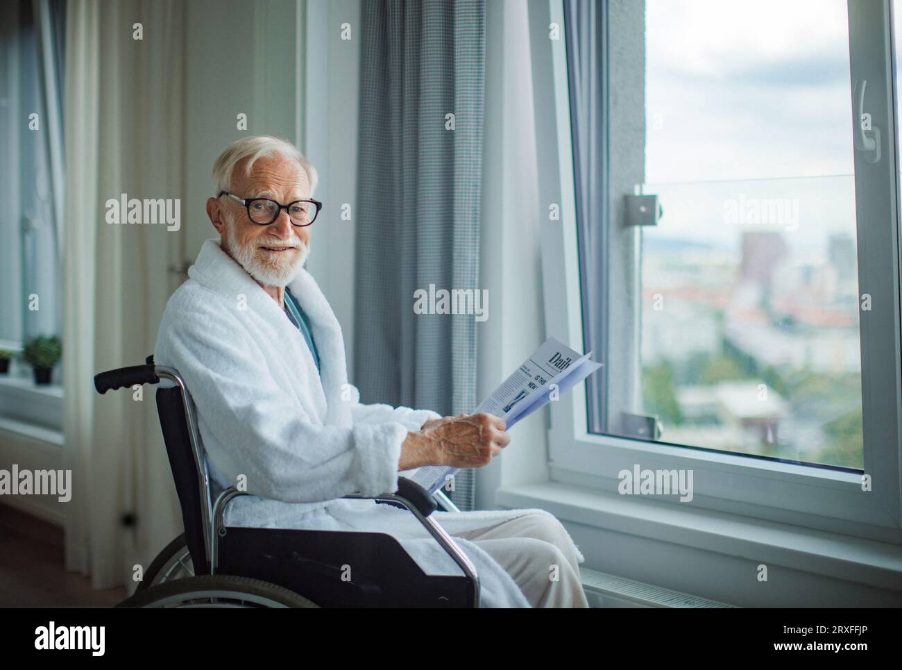 Älterer Mann im Rollstuhl, der am Morgen die Zeitung in seinem Gewand liest. Stockfoto