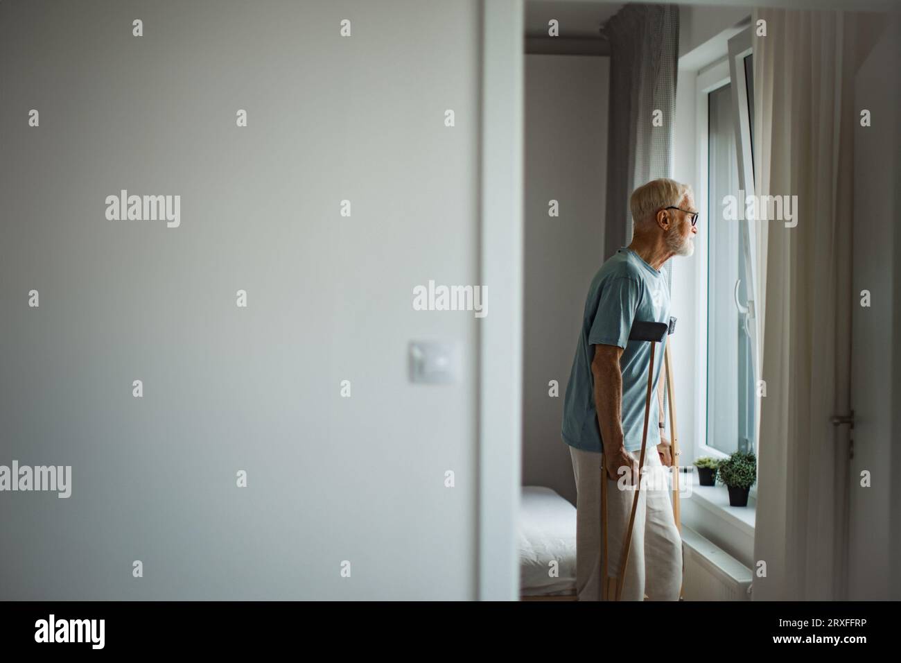 Älterer Mann mit Krücken, der Zeit allein in seiner Wohnung verbringt. Stockfoto