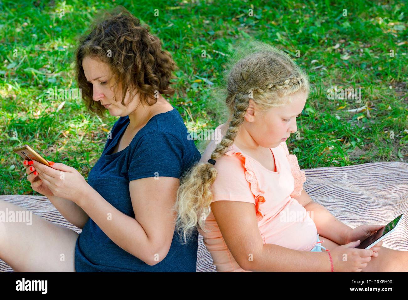 Mutter und Tochter mit Gadgets. Die Frau und das Kind halten das Smartphone, Tablets. Das Konzept Freizeit für Familien auf Picknick. Mangelnde Kommunikation Stockfoto