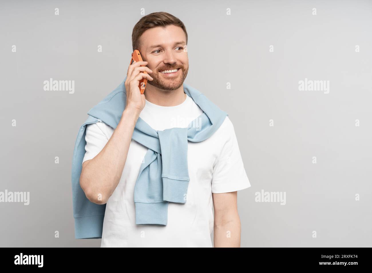 Glücklicher positiver Mann mittleren Alters, der auf Smartphone isoliert auf grauem Hintergrund spricht. Stockfoto