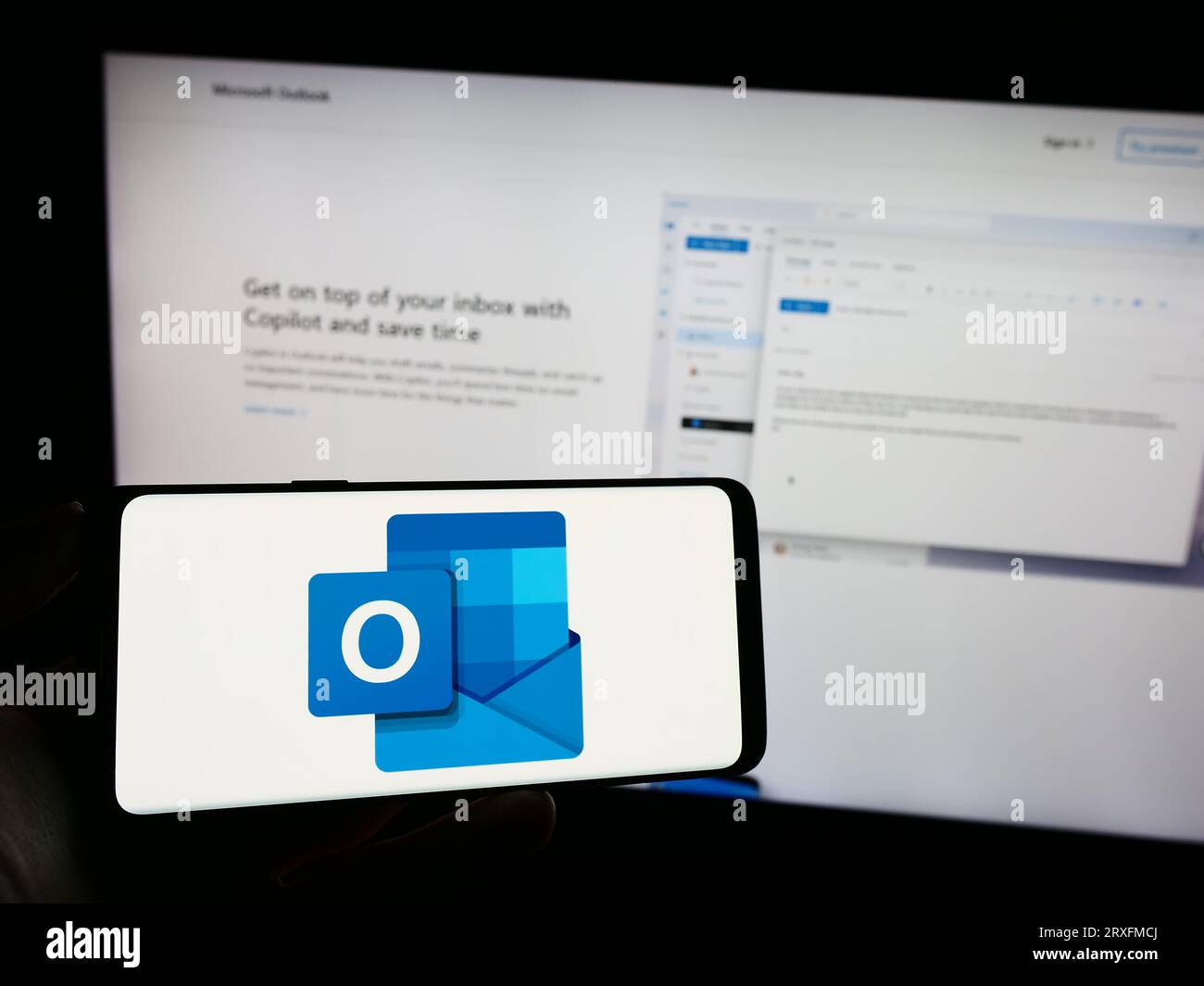 Person, die ein Mobiltelefon mit dem Logo der E-Mail-Software Microsoft Outlook auf dem Bildschirm vor der Firmenwebseite hält. Konzentrieren Sie sich auf das Display des Telefons. Stockfoto
