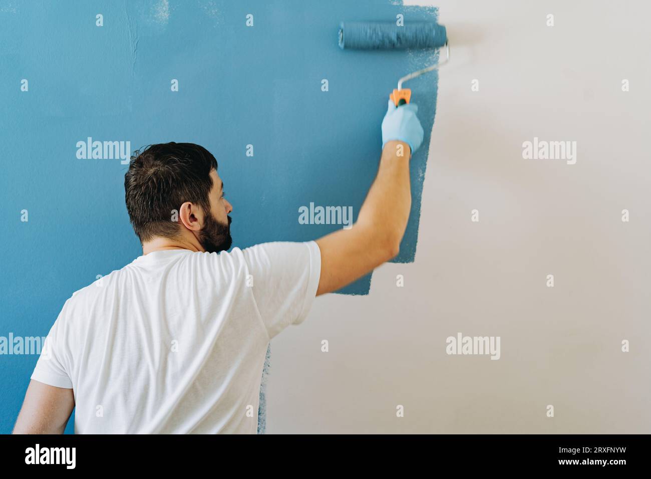 kaukasischer bärtiger Mann malte Wand mit Malerwalze. Malerwohnung, renovierendes Haus mit blauer Farbe. Bild mit selektivem Fokus Stockfoto