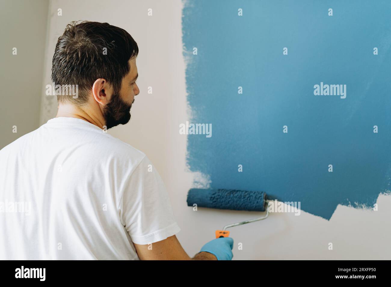 kaukasischer bärtiger Mann malte Wand mit Malerwalze. Malerwohnung, renovierendes Haus mit blauer Farbe. Bild mit selektivem Fokus Stockfoto