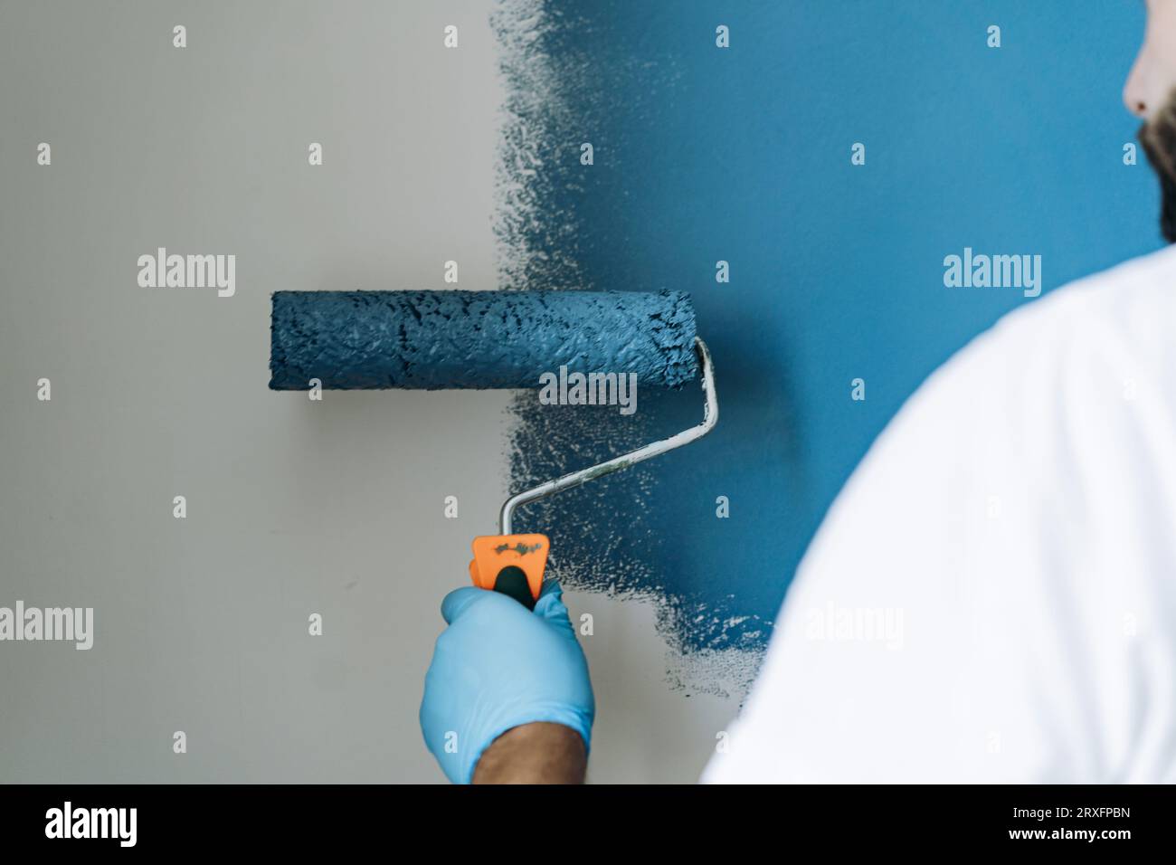 kaukasischer bärtiger Mann malte Wand mit Malerwalze. Malerwohnung, renovierendes Haus mit blauer Farbe. Bild mit selektivem Fokus Stockfoto