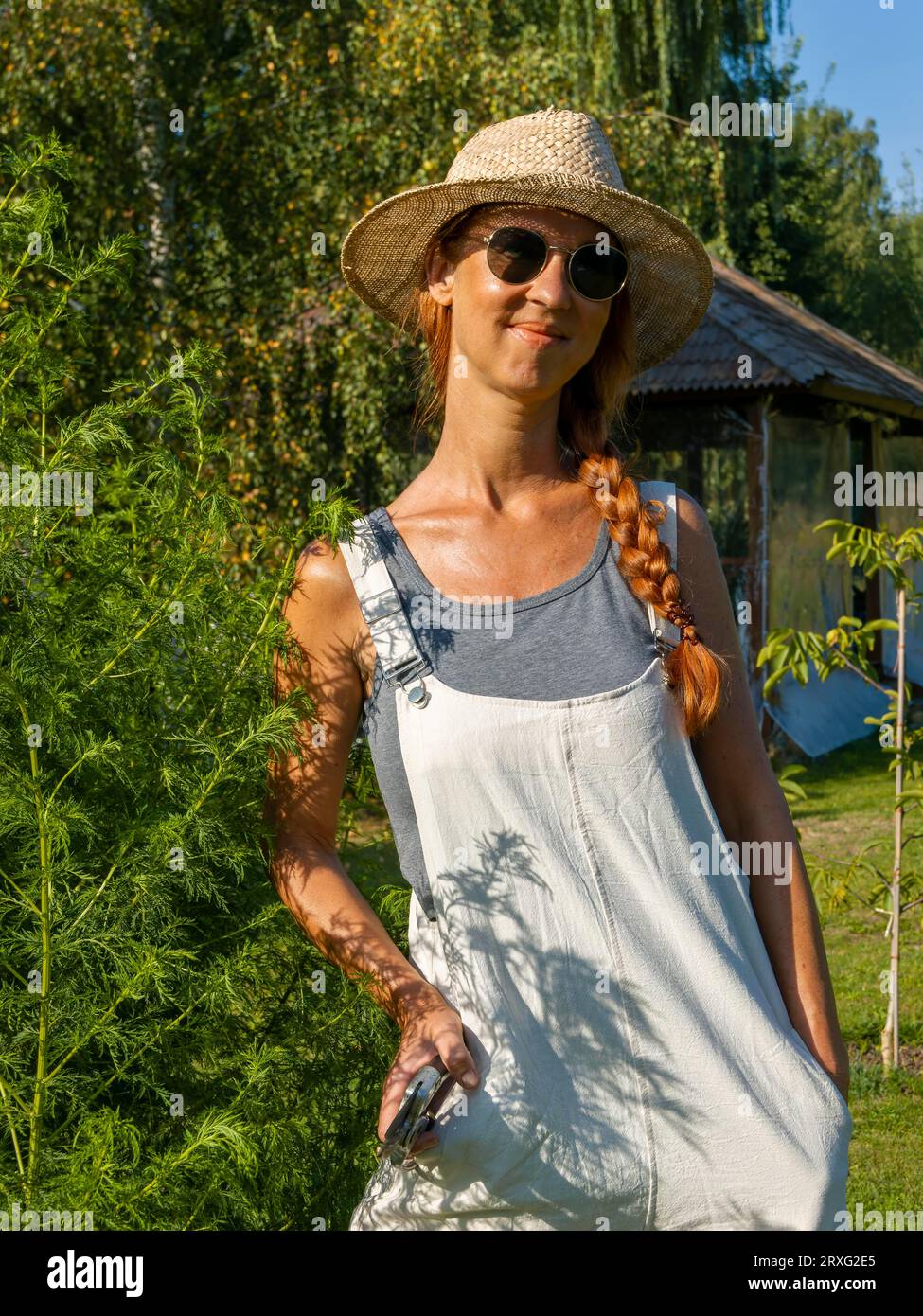 Frau im Kräuterbett, Heilkräuter im Garten, Gartenarbeit im Kräutergarten mit Strohhut und Sonnenbrille, Deutschland Stockfoto