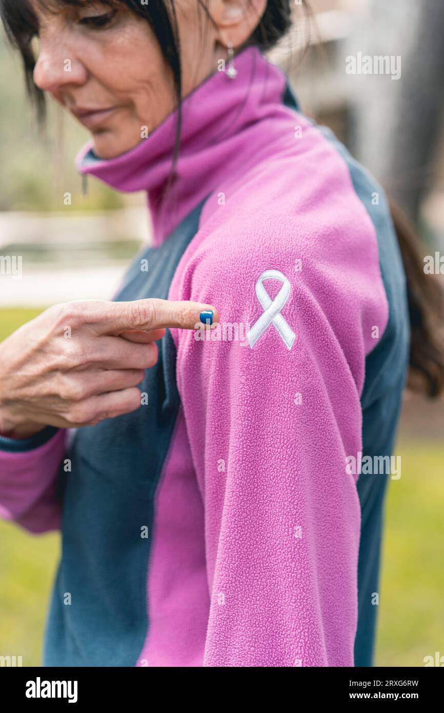 Eine Erwachsene Frau, die mit dem Finger auf ihrem Sweatshirt auf ein gesticktes Band zur Krebswahrnehmung zeigt. Vertikale Aufnahme Stockfoto