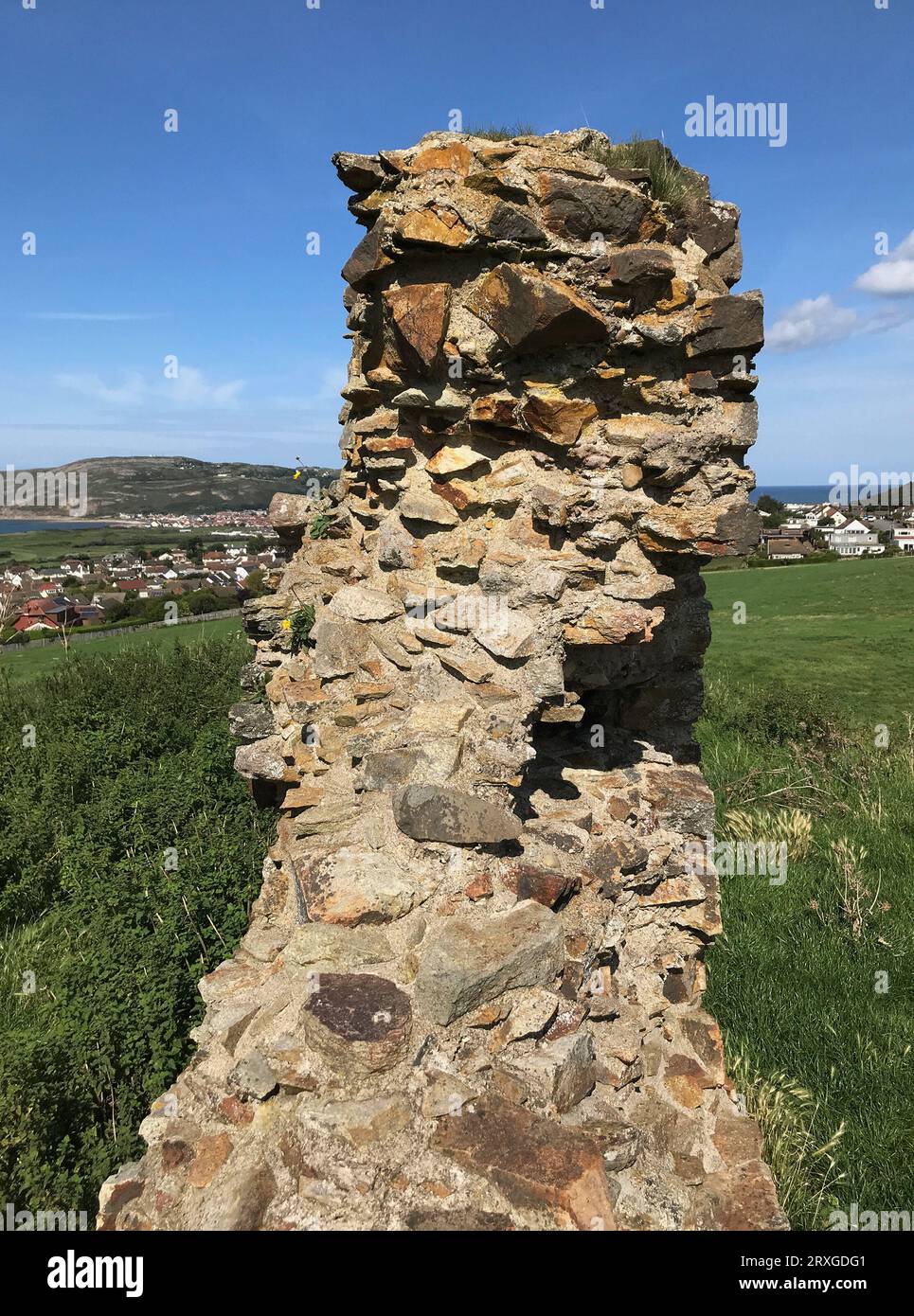 Blick auf die Ruinen des Eingangs von Deganwy Castle, Wales, die einen Felsen aus ordovizischem rhyolitischem Tuffstein überragen und in der Ferne in Richtung Llandudno blicken Stockfoto