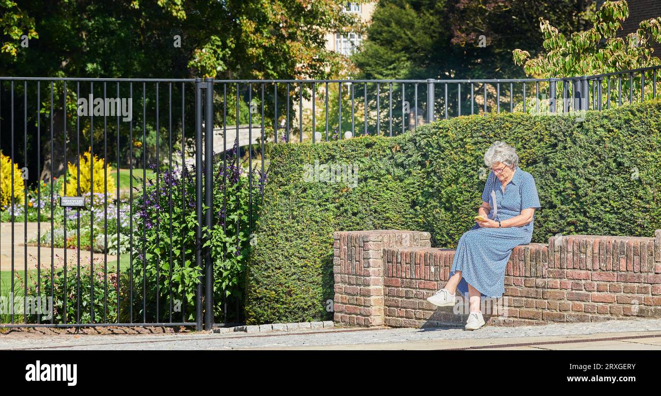 Eine einsame Touristenfrau sitzt an einem sonnigen septembertag auf einer Mauer vor dem Queens College, University of Cambridge, England. Stockfoto