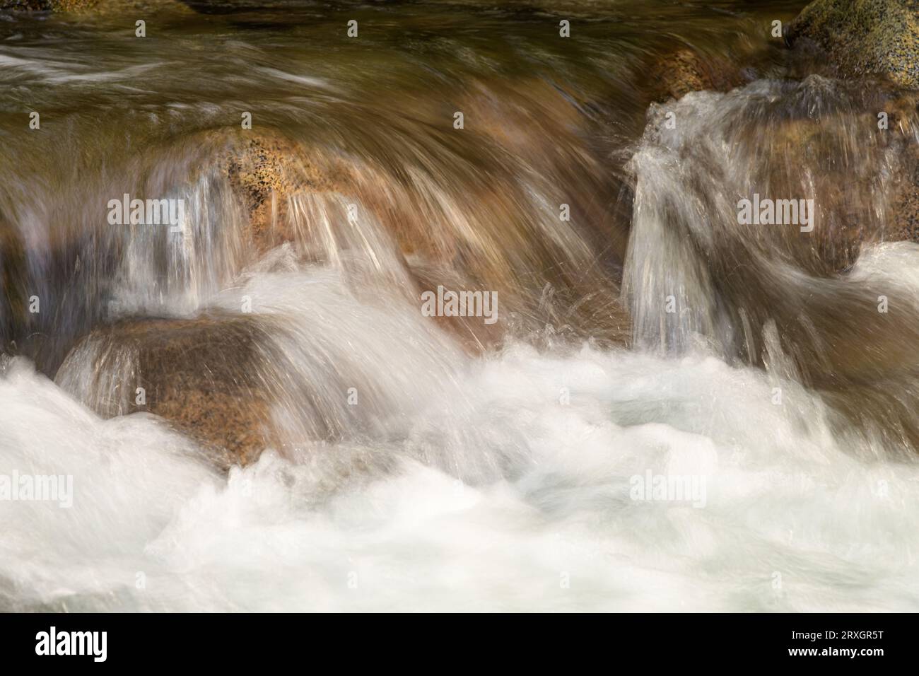 Der Gebirgsbach stürzt über Flussfelsen mit weißem Wasser und braunen Farbsteinen in Nahaufnahme Stockfoto