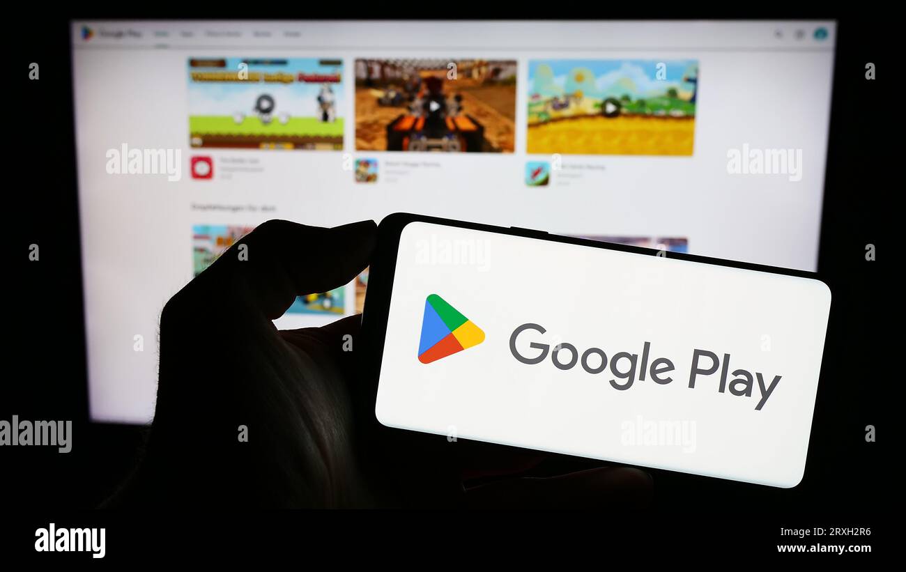 Person, die ein Mobiltelefon mit dem Logo der App-Distributionsplattform Google Play auf dem Bildschirm vor der geschäftlichen Webseite hält. Konzentrieren Sie sich auf das Display des Telefons. Stockfoto