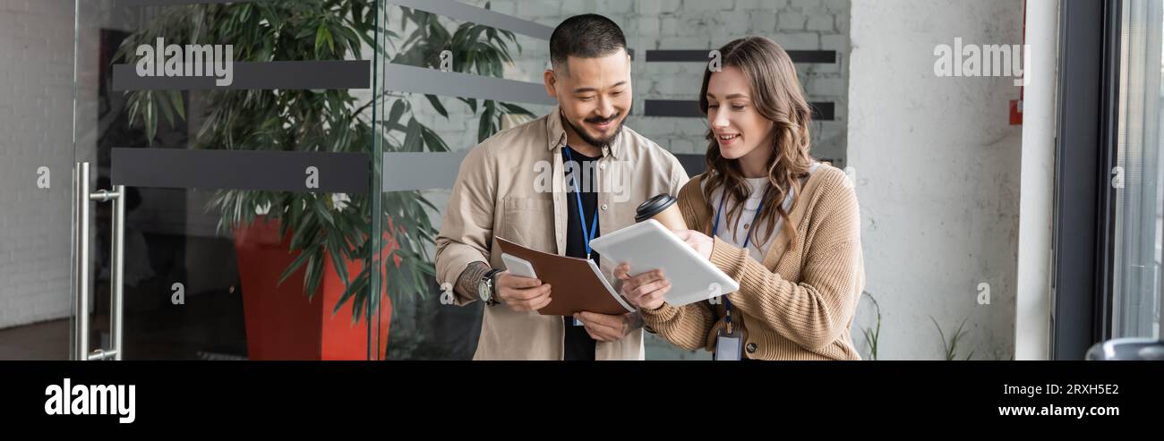 Glückliche Geschäftsfrau, die einem asiatischen Kollegen im modernen Büro ein Tablet mit Startup-Projekt zeigt, Banner Stockfoto