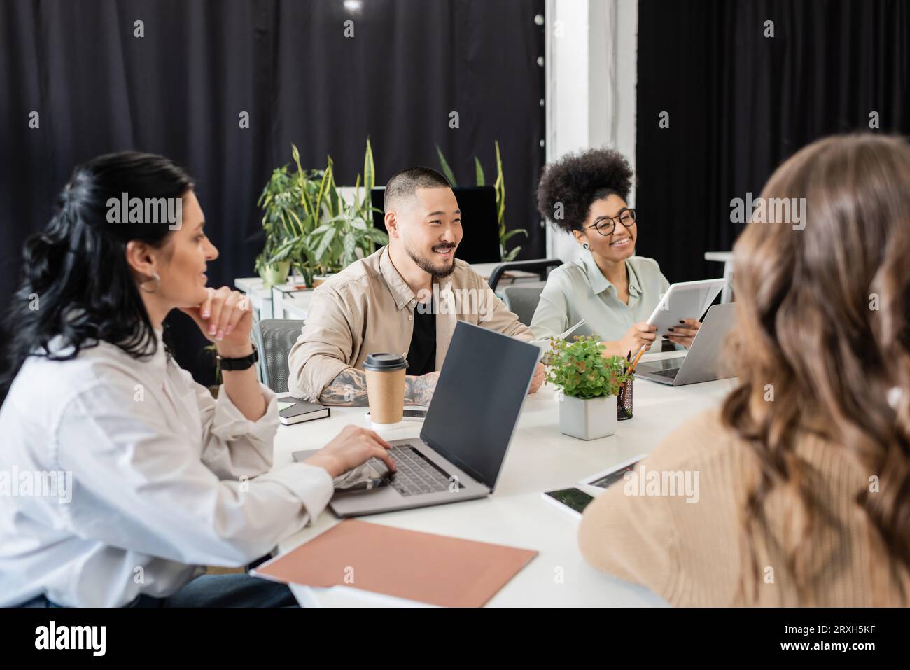 Fröhliche, multikulturelle Geschäftsleute, die Projekte diskutieren und Ideen mit Teamleitern im Büro austauschen Stockfoto