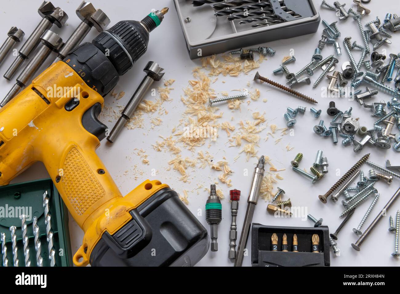 Hintergrund eines elektrischen Akku-Bohrers mit Bohrern sowie verschiedenen Befestigungsteilen und Holzspänen. Stockfoto