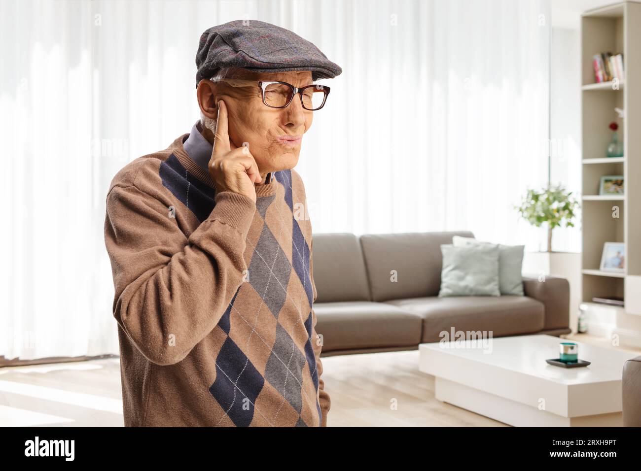 Älterer Mann, der sein Ohr vor einem unangenehmen Geräusch zu Hause im Wohnzimmer schützt Stockfoto