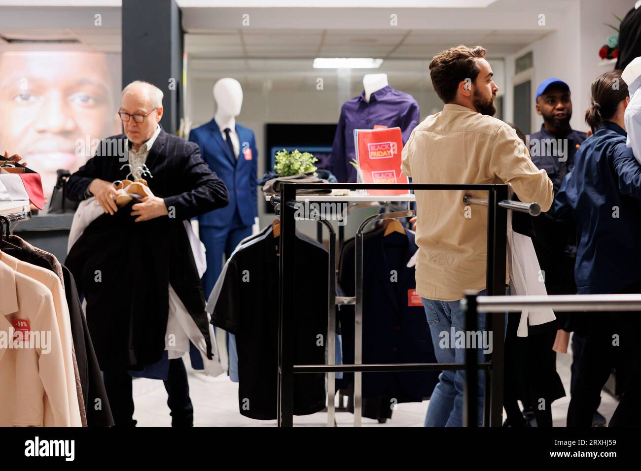 Leute, die während des Black Friday-Verkaufs nach Angeboten in einem lokalen Bekleidungsgeschäft suchen, besessene Kunden, die sich Kleidung zu ermäßigten Preisen schnappen, suchen nach Schnäppchen im Modegeschäft. Schnäppchenjagd Stockfoto