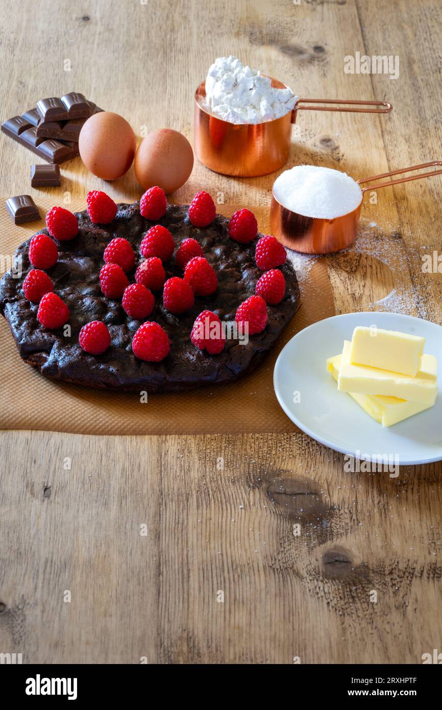 Schokoladen- und Himbeerkuchen mit Zutaten auf einem Holztisch Stockfoto