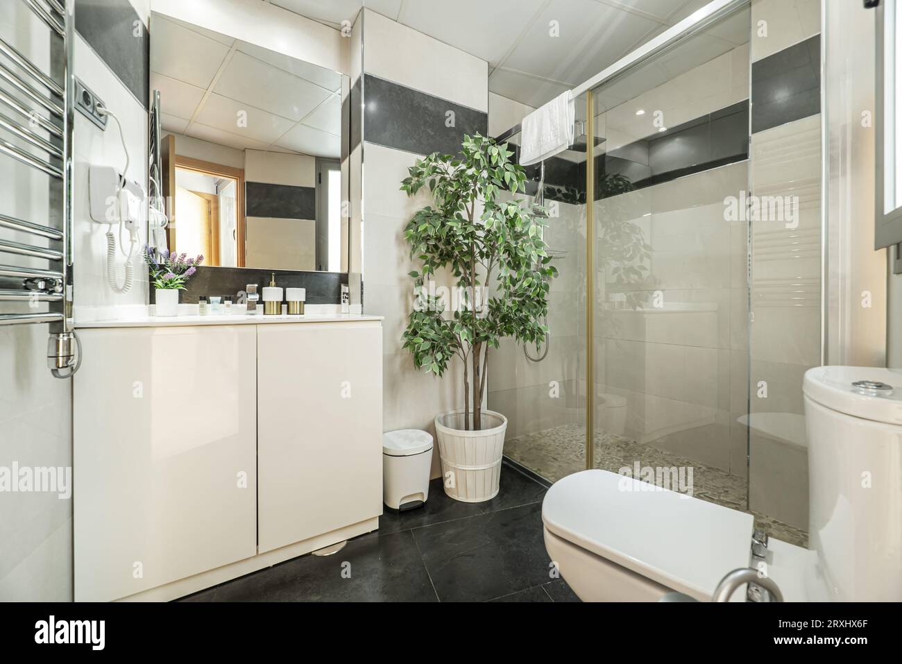 Großes Badezimmer mit Holzschrank mit feinem Porzellanwaschbecken, Duschkabine mit Glasscheiben, verchromtem Handtuchkühler und rahmenlosem Spiegel an der Wand Stockfoto
