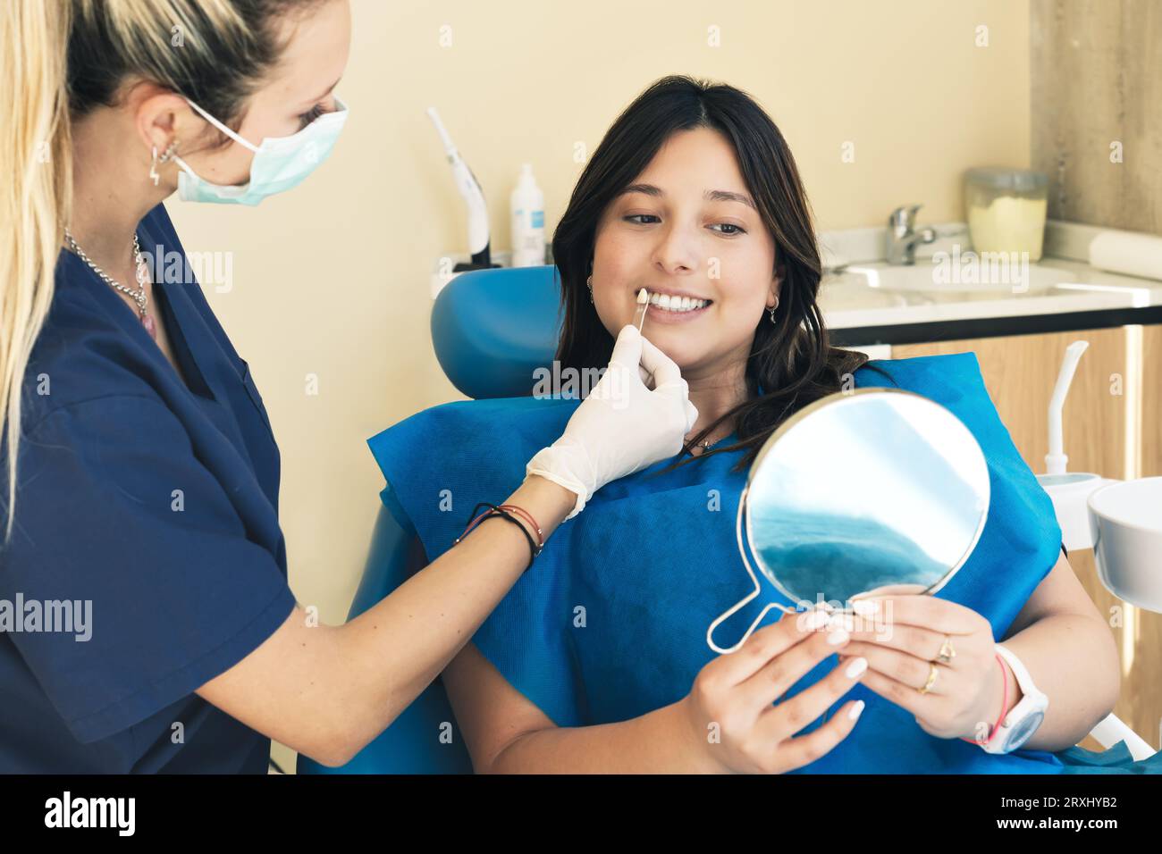 Zahnärztin-Farbkontrolle der Zahnfarbe von Patientinnen mit Zahnschmelzskala, zahnärztliche Praxiseinrichtung. Die junge Frau lächelt auf dem Zahnarztstuhl Stockfoto