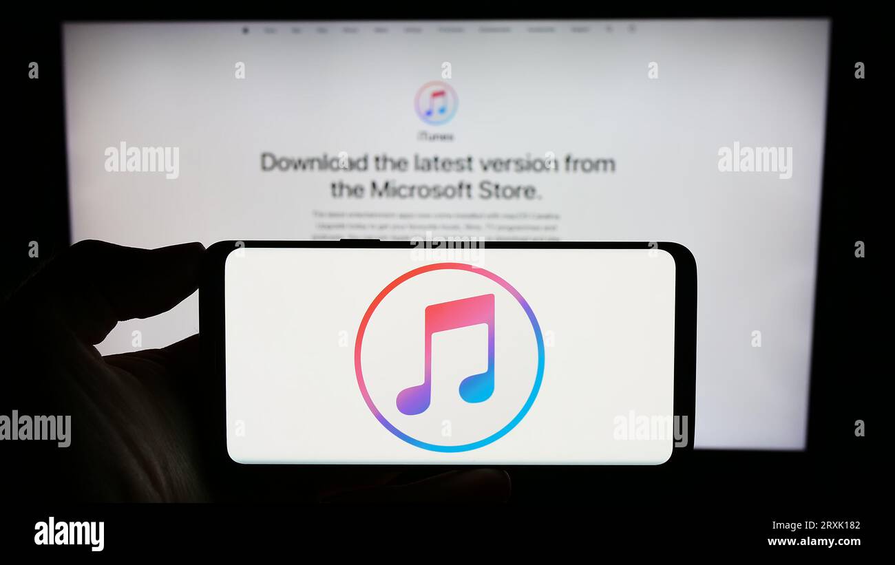 Person, die ein Mobiltelefon mit dem Logo des Mediensoftwareprogramms Apple iTunes auf dem Bildschirm vor der Firmenwebsite hält. Konzentrieren Sie sich auf das Display des Telefons. Stockfoto