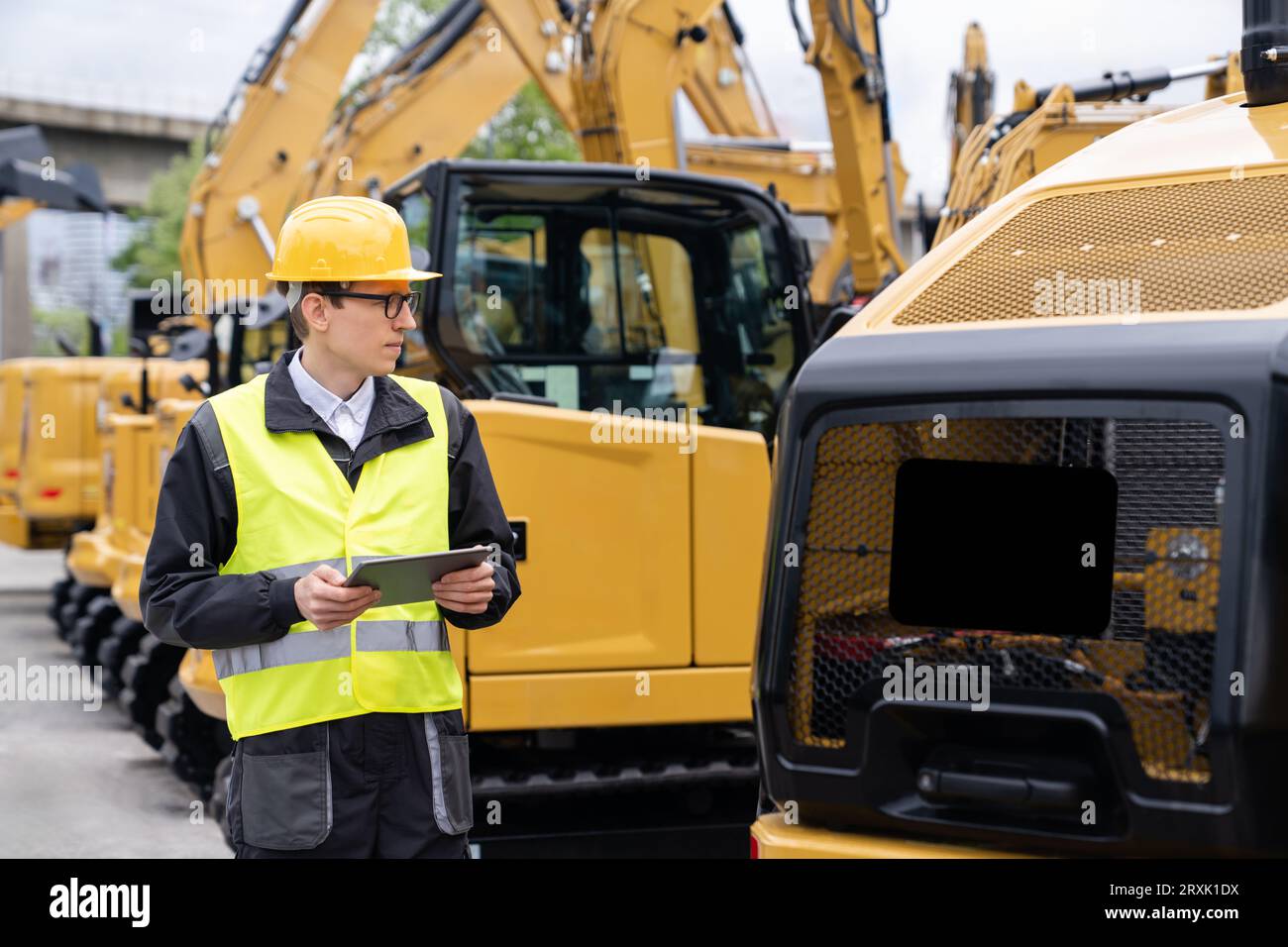 Ingenieur mit Helm und digitalem Tablet steht neben Baubaggern. Stockfoto