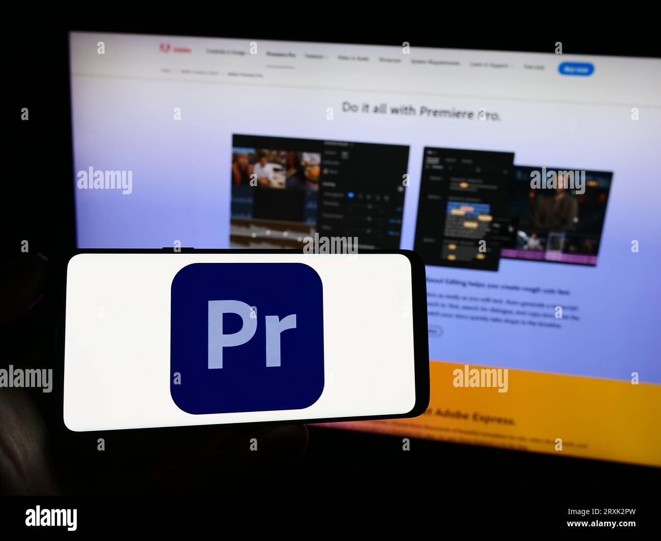 Person, die ein Mobiltelefon mit dem Logo der Videobearbeitungssoftware Adobe Premiere Pro auf dem Bildschirm vor der Webseite hält. Konzentrieren Sie sich auf das Display des Telefons. Stockfoto