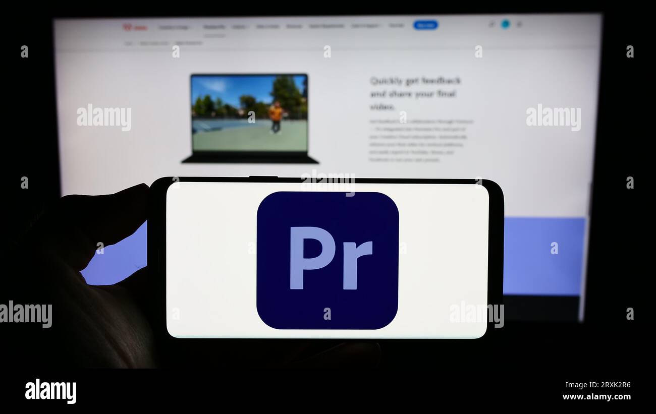 Person, die ein Mobiltelefon mit dem Logo der Videobearbeitungssoftware Adobe Premiere Pro auf dem Bildschirm vor der Firmenwebseite hält. Konzentrieren Sie sich auf das Display des Telefons. Stockfoto