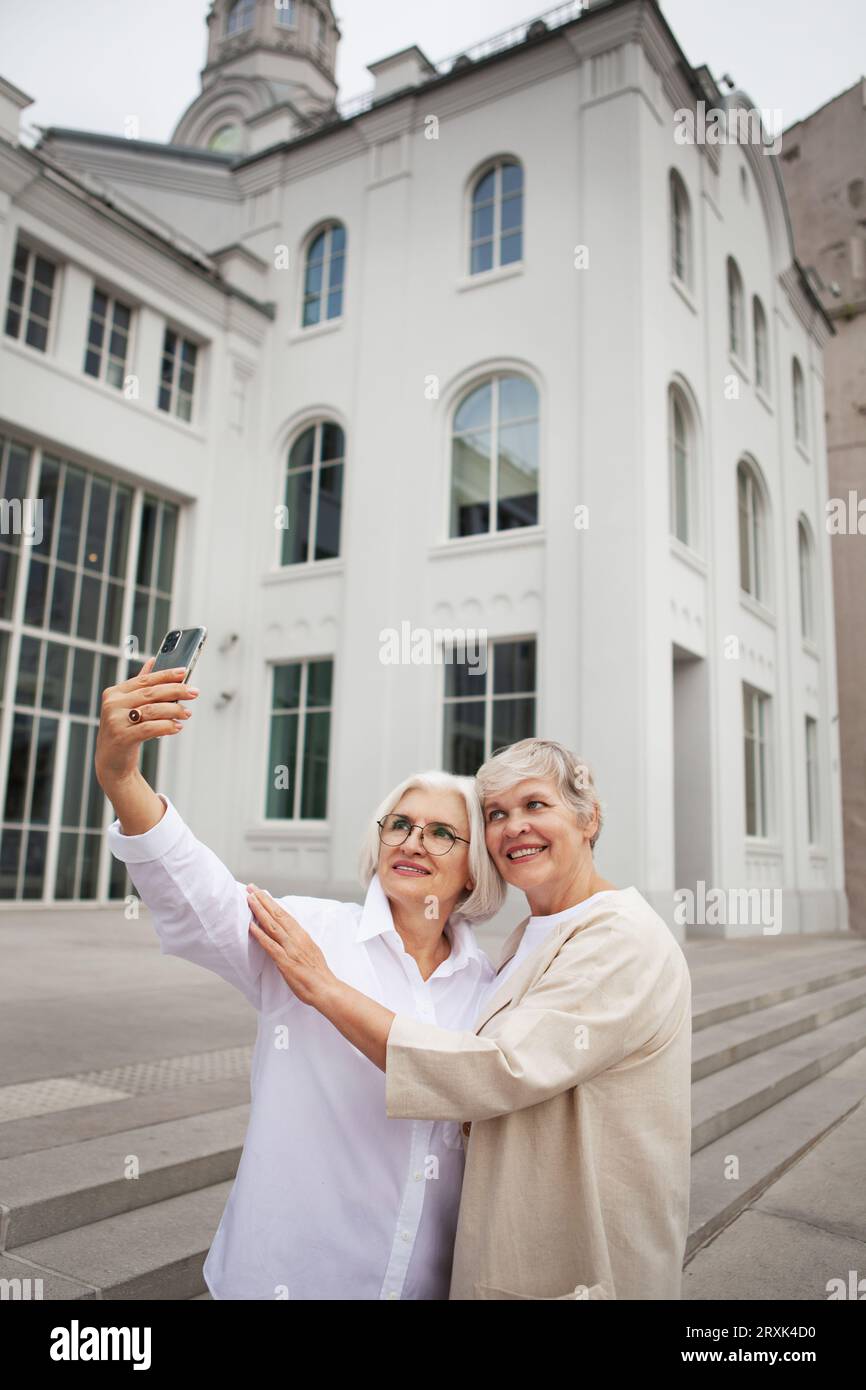 Glückliche Seniorinnen mit grauen Haaren machen Selfie-Fotos auf dem Handy im Freien in der Stadt, lächeln und genießen sich selbst. Zwei pensionierte Freundinnen Stockfoto